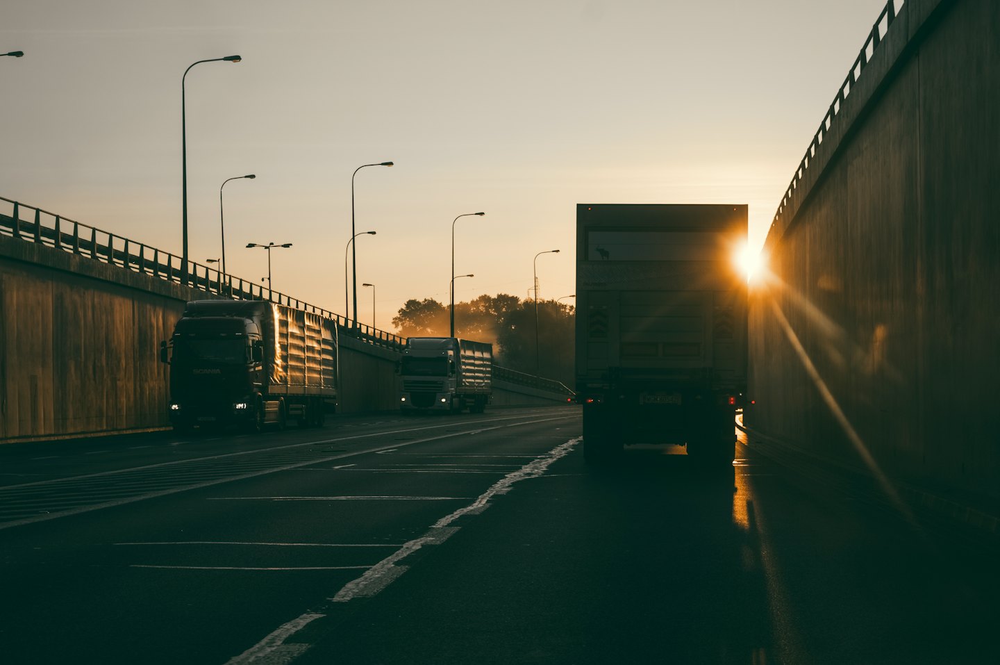 Camiones de carga circulan por una autopista de varios carriles al atardecer.