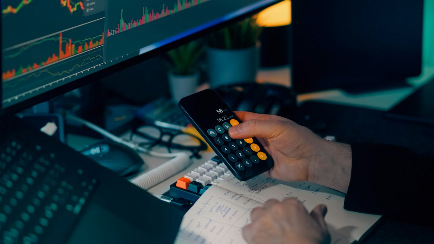 Manos usando una calculadora de smartphone sobre un cuaderno financiero.
