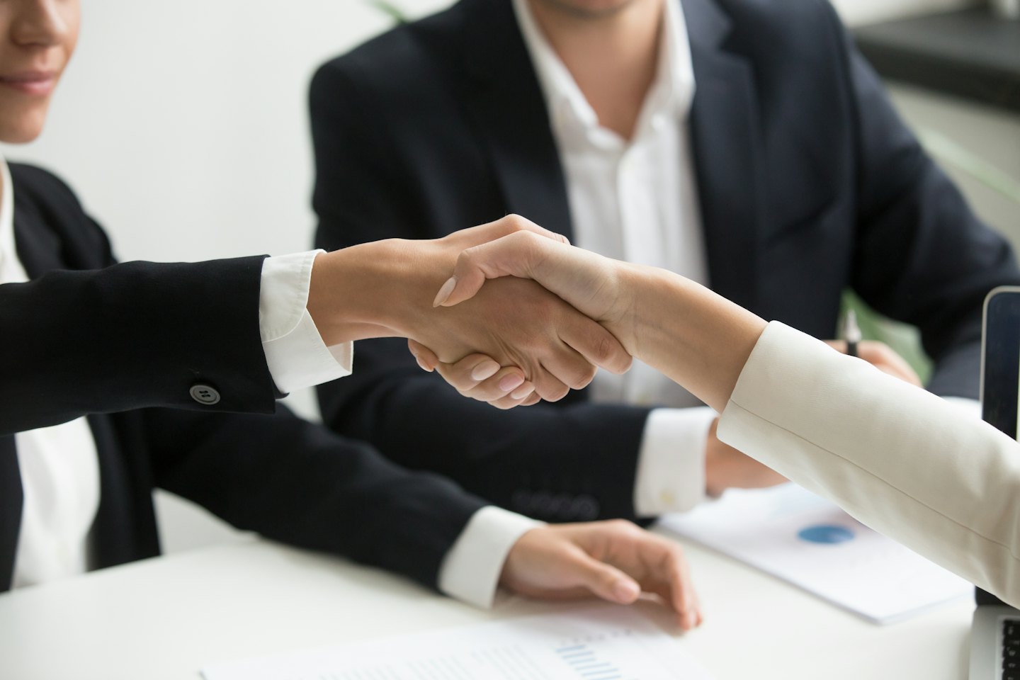 Dos profesionales de negocios se dan la mano sobre un escritorio en una oficina.