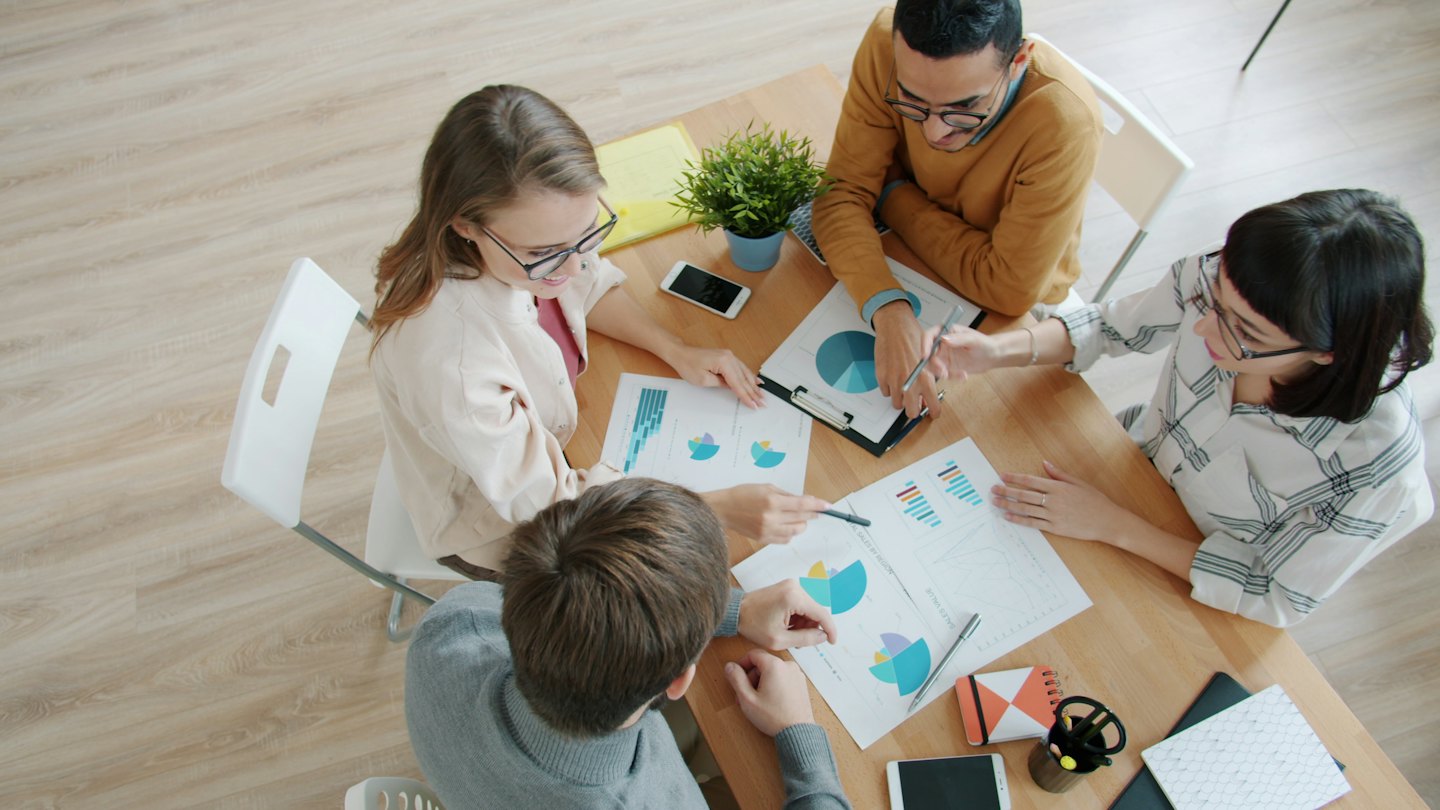Un equipo diverso de negocios colabora sobre gráficos financieros en una mesa.