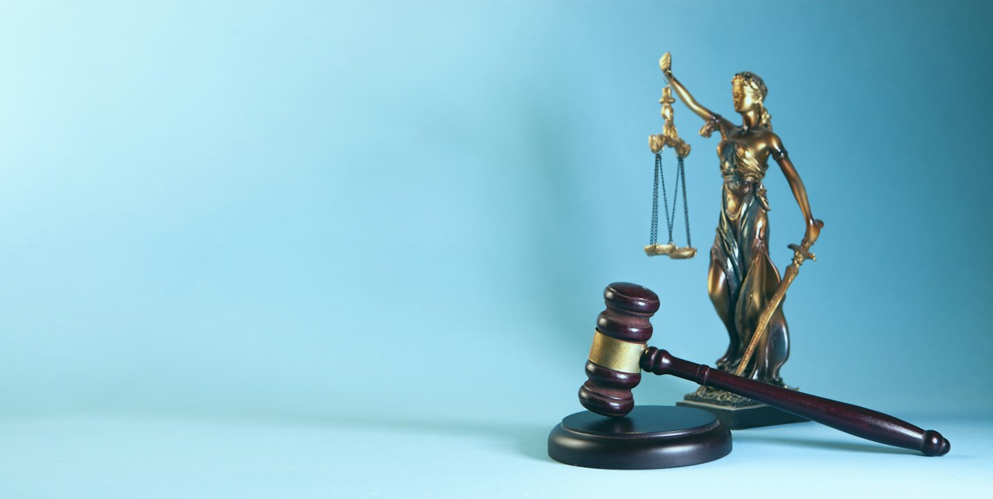 Estatua de bronce de la Dama de la Justicia con balanza y espada cerca de un mazo de madera.